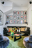 Picture wall of posters above grey sofa with glass topped coffee table in North London home UK