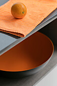 Orangefarbenes Geschirrtuch mit Schale auf grauem Regal in einer Küche in London, UK