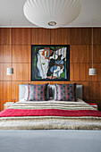Moderne Kunst über einem Doppelbett mit Kissen und Holzvertäfelung in einer Wohnung in London UK