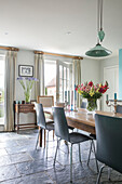 Dining chairs at wooden table with cut flowers and green pendant in Hampshire home England UK