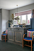 Pendant light above sideboard with pair of blue chairs in window of Hampshire home England UK