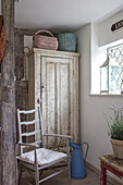 Baskets on vintage French cupboard with chair at window in Surrey farmhouse UK