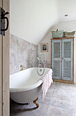 Cupboard made of salvaged shutters with freestanding bath in Surrey farmhouse UK