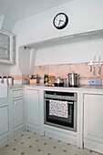 Uhr über dem Ofen mit Pfannen auf dem Kochfeld und Wänden in Pavilion Grey in einer Küche in Wiltshire UK