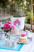 PInk roses and sponge cake with cups on table in Wiltshire garden UK