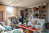 Geblümte Sofas und Ohrensessel mit Bücherregalen in einem Bauernhaus in Norfolk UK