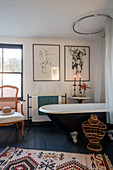 Pencil sketches and wicker chair with black bath and painted floorboards in Norfolk farmhouse UK