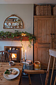 Wooden furniture with mirror and garland above lite fire in Georgian Hampshire cottage dining room UK