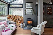 Sessel und Sofa mit Holzstapeln und Kaminfeuer im Wintergartenanbau einer Londoner Villa UK