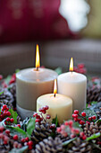 Three lit candles in garland of pine cones and berries Hampshire UK