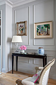 Lamp on console with framed artwork in panelled living room London UK