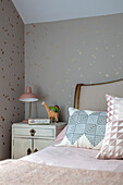 Lamp on bedside table with geometric cushions on star wallpaper Sussex UK