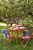 Red table and chairs under apple tree with bunting in Isle of Wight garden UK