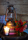 Lit candle and cut flowers with hurricane lamp on books in Autumn UK