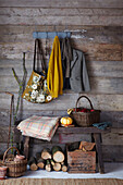 Rustic wooden panelling with coat rack filled with jacket scarf and jumper a bench with pumpking and a blanket and basket filled with red apples