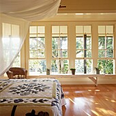 Hauptschlafzimmer mit Holzfußboden und großen Fenstern Doppelbett mit Patchwork-Bettdecke