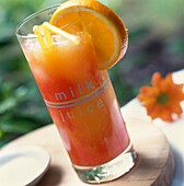 Orange and cranberry juice in a glass on a tabletop in a garden