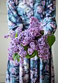 Person in floral dress holding a bunch of purple lilac flowers