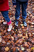 Mädchen und Junge in Gummistiefeln stehen auf nassem Herbstlaub, niedriger Abschnitt, Haslemere, Surrey, England