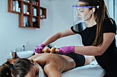 Masseuse massaging client wearing gloves and face visor