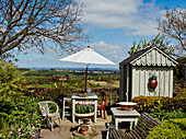 Sitzplatz vor Gerätehäuschen in sonnigem Garten mit Landschaftsblick