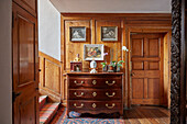 Antique chest of drawers in front of wood panelled wall in a stairwell