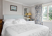 Bedroom with light-colored bed linen and patterned curtains at the window