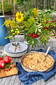 Garden table with apple crumble, pile of plates and autumnal decorations