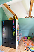 Children's room with sloping ceiling, black wardrobe, colourful rug and toy storage