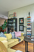 Living room with yellow sofa, stack of books and modern wall art