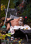 Dog on deckchair with cushion and blanket next to rake and thermos flask in autumn