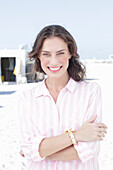 A brunette woman wearing a pink striped blouse on a beach
