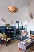 Wooden slatted pendant light above reading area with vintage furniture and fireplace