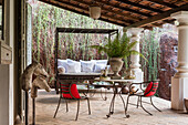 Überdachte Terrasse mit Vintage-Metalltisch und roten Stühlen
