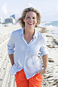 A blonde woman wearing a light-blue striped shirt and orange shorts on a beach