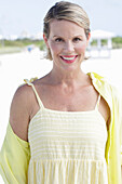 Blonde Frau in gelbem Top mit dünnen Trägern und gelbem Hemd am Strand