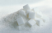 A heap of caster sugar and nine sugar cubes on a white background