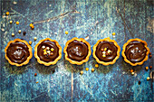 A row of chocolate caramel tarts topped with sprinkles and sea salt