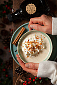 Pair of hands around a mug of gingerbread latte topped with whipped cream and cookie crumbs.