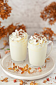 Two glasses of white hot chocolate with cream and bronze sprinkles