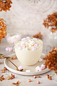 A glass of white hot chocolate with cream and marshmallows