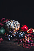 Herbstliches Stillleben mit Kürbis, Granatapfel und Weintrauben vor dunklem Hintergrund
