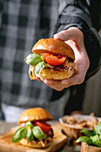 Hand hält Mini-Burger mit geschmortem Rindfleisch, Tomaten und Basilikum