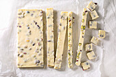 Sliced strips and squares homemade white chocolate candy bar with pistachios nuts and cranberries