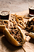 Cheesesteaks and fries on parchment paper with glasses of dark beer