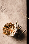 A small bowl of toothpicks on the edge of a table with a few scattered on the table