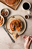 Hands building a stack of maple pecan pancakes with caramelized bananas on a plate
