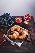 Frühstücksszene mit Croissants, Kaffee, Weintrauben und Granatapfel
