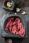 Raw beef fillet on black stone plate and mortar with herbs