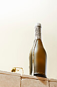 Bottle of champagne bubbling over onto a bright, tile surface with cream background